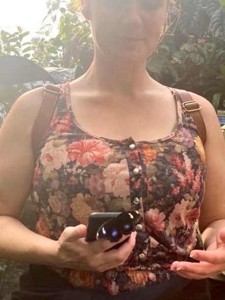 Lady in a butterfly sanctuary holding a phone with a butterfly sitting on it