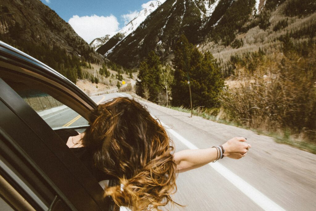 Lady with head out of the window on a road and the wind blowing in her hair from the back