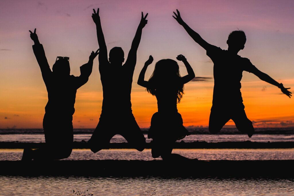 Family of four jumping on the beach as silhouettes against a sunset demonstrating off grid family of worldschoolers roadschoolers